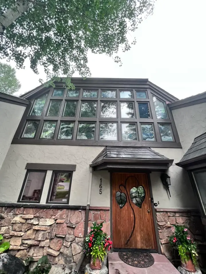 Mountain home exterior with a stone base, stucco walls, a large multi-pane window wall and a carved wood entry door under a small awning